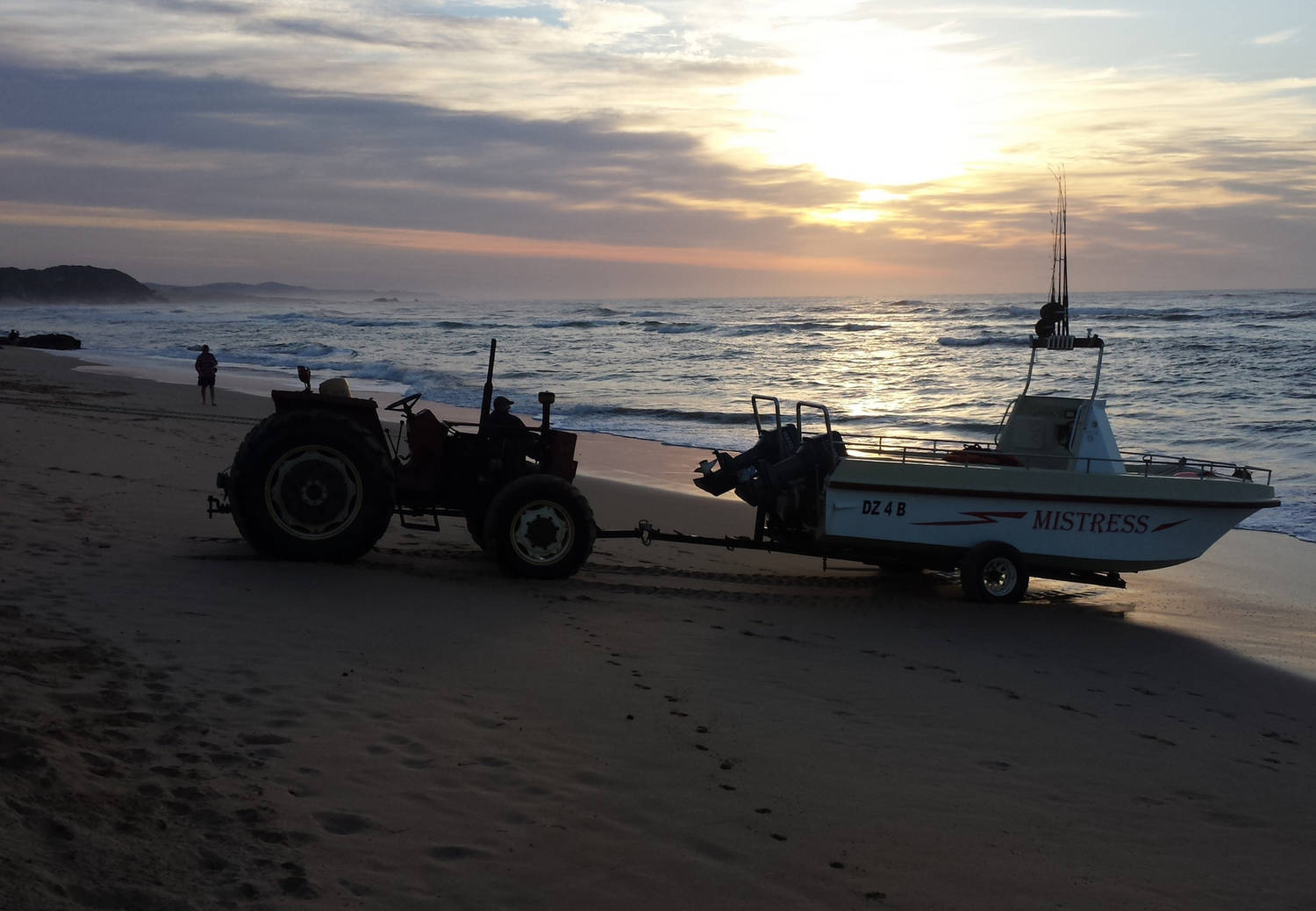 A photograph of a boat being towed on a beach near the sea shore at sunrise